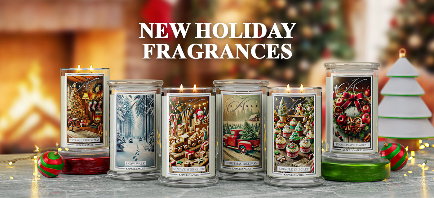Assorted holiday candles with festive designs on a wooden surface, with a blurred Christmas scene in the background.