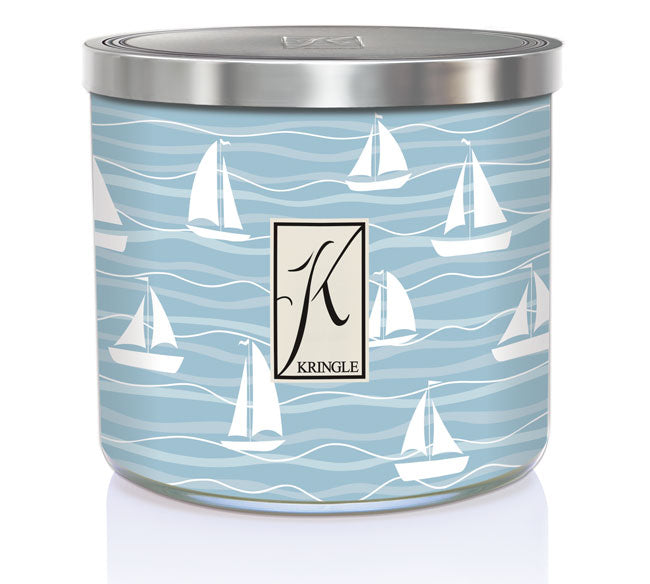 A candle in a metal tin with a light blue design of sailboats and waves. The label reads