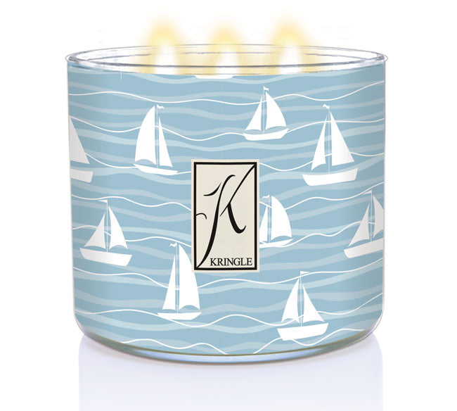 Light blue candle with white sailboat design, three lit wicks, and a "K" logo with the text "Kringle" on the front.