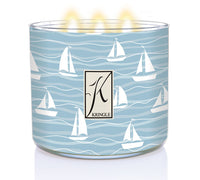 Light blue candle with white sailboat design, three lit wicks, and a "K" logo with the text "Kringle" on the front.