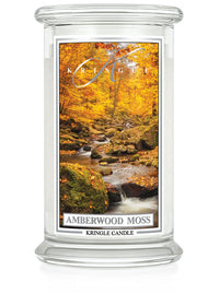 Unlit Amberwood Moss candle with two wicks. Label shows a forest stream surrounded by autumn trees and mossy rocks.