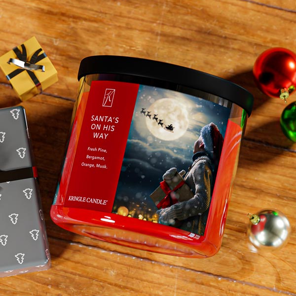 Kringle Candle Christmas-themed candle packaging on a wooden surface with festive decorations.