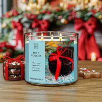 Candle with a festive design featuring cookies and a red bow, set against a blurred Christmas-themed background.
