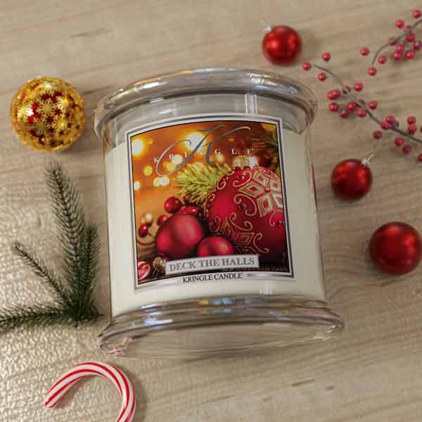 Kringle Candle 'Deck the Halls' on a wooden surface with Christmas decorations.
