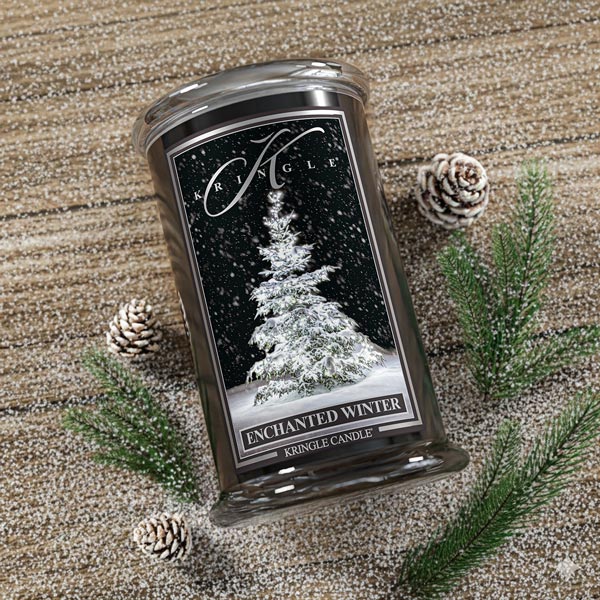 Kringle Candle Enchanted Winter candle on a textured surface with pinecones and branches.