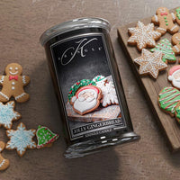 Kringle Candle with gingerbread-themed packaging surrounded by decorated cookies on a wooden surface