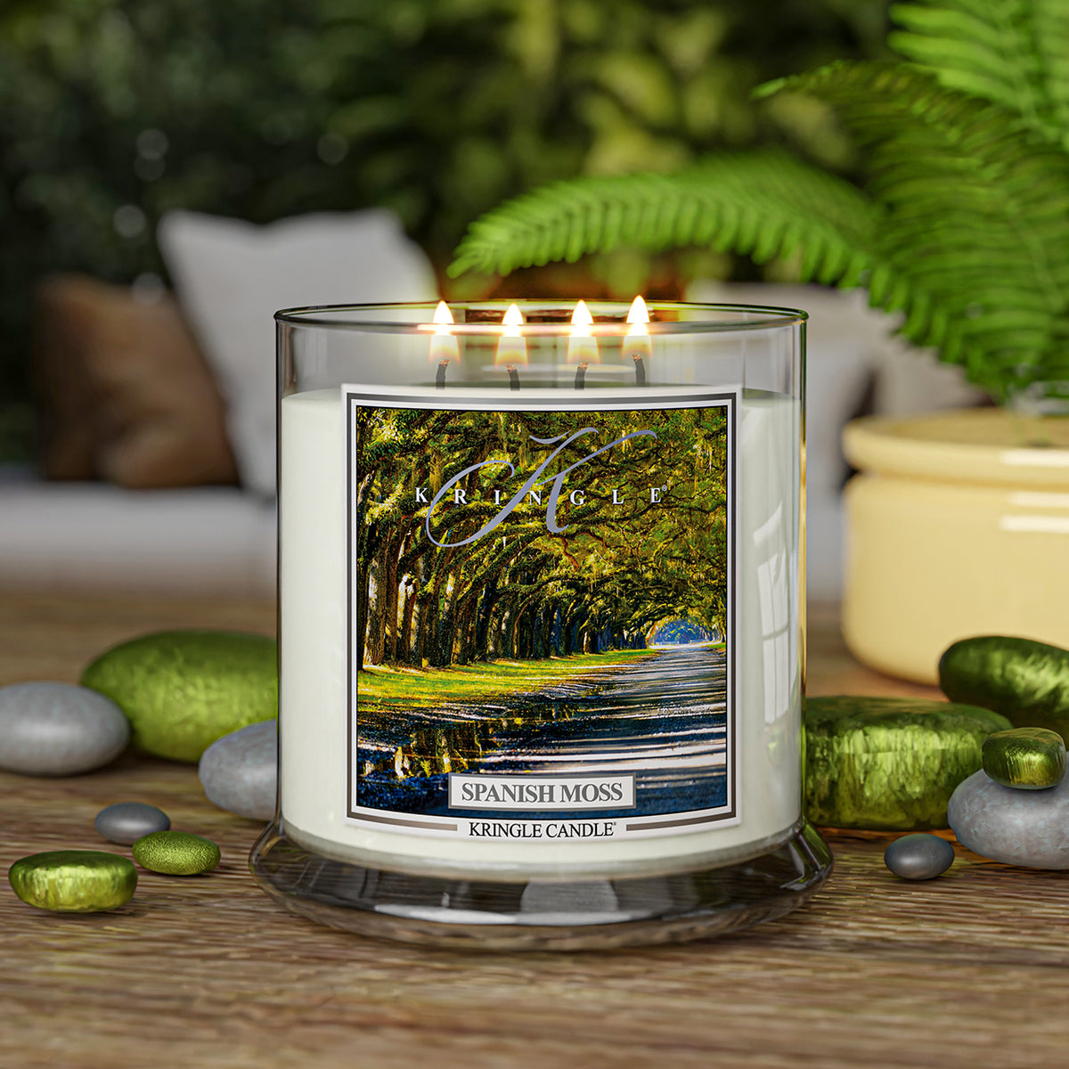 A lit candle jar with a label showing a tree-lined path. It reads "Spanish Moss, Kringle Candle."