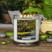 A lit candle jar with a label showing a tree-lined path. It reads "Spanish Moss, Kringle Candle."