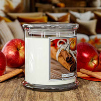 Spiced apple candle in a glass jar with apples and cinnamon sticks on a wooden surface