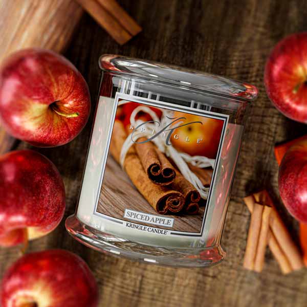 Spiced Apple Kringle Candle surrounded by apples and cinnamon sticks on a wooden surface