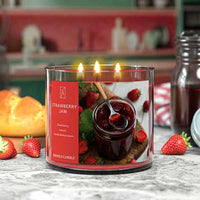 Three-wick candle labeled 'Strawberry Jam' with a jar of jam and strawberries on the label, placed on a marble surface.
