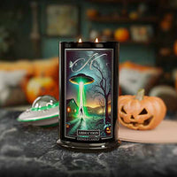 Candle with alien abduction design on a Halloween-themed table with pumpkins and a UFO.
