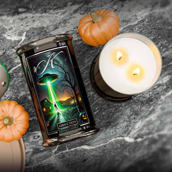 Candle with a label featuring a green alien landscape on a dark surface with pumpkins.