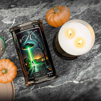 Candle with a label featuring a green alien landscape on a dark surface with pumpkins.