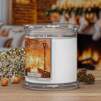 White candle in a glass jar with a decorative label on a wooden surface, with a blurred background of a cozy room.