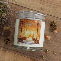 Candle in a glass jar with a decorative label on a wooden surface with pine cones and acorns.