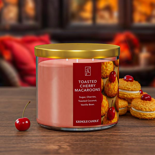 Kringle Candle Toasted Cherry Macaroons candle with a cherry and cookies on a wooden surface.