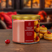 Kringle Candle Toasted Cherry Macaroons candle with a cherry and cookies on a wooden surface.