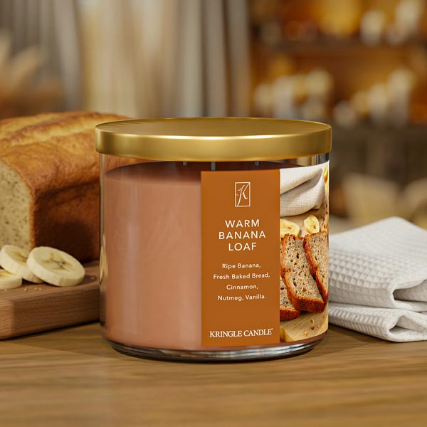 Kringle Candle 'Warm Banana Loaf' candle on a wooden surface with bread and bananas in the background