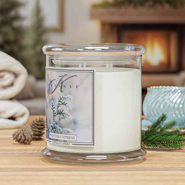 Kringle Candle Winter Cypress  4-wick candle on a table with a fireplace in the background