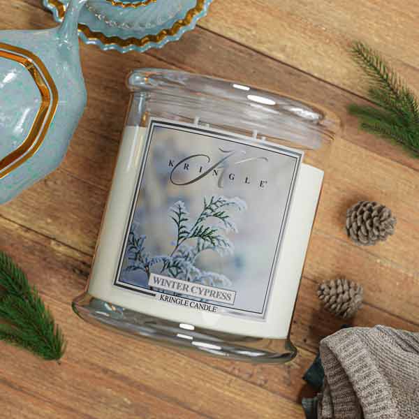 Kringle Candle Winter Cypress candle on a wooden surface with decorative elements.