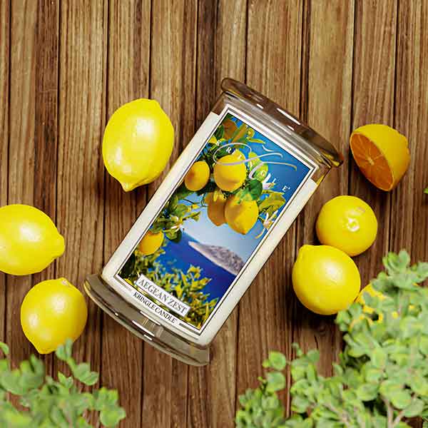 Kringle Candle Aegean Zest Large Jar Candle – A clear glass jar candle with a white wax interior, featuring a label with bright yellow lemons, green leaves, and white blossoms set against a deep blue ocean and an island in the background. The label includes the ‘Kringle Candle’ logo at the top, the fragrance name ‘Aegean Zest’ in bold, and ‘Kringle Candle’ branding at the bottom.