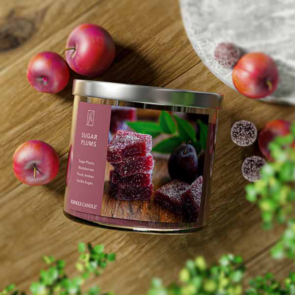 A three-wick candle in a clear glass jar with a silver lid and a festive holiday-themed label. The label features a bowl of sugared plums and juicy blackberries, dusted with powdered sugar. The candle’s wax is deep purple, and the wicks are unlit. The scent notes listed are sugared plums, blackberries, delicate florals, amber, and vanilla sugar.