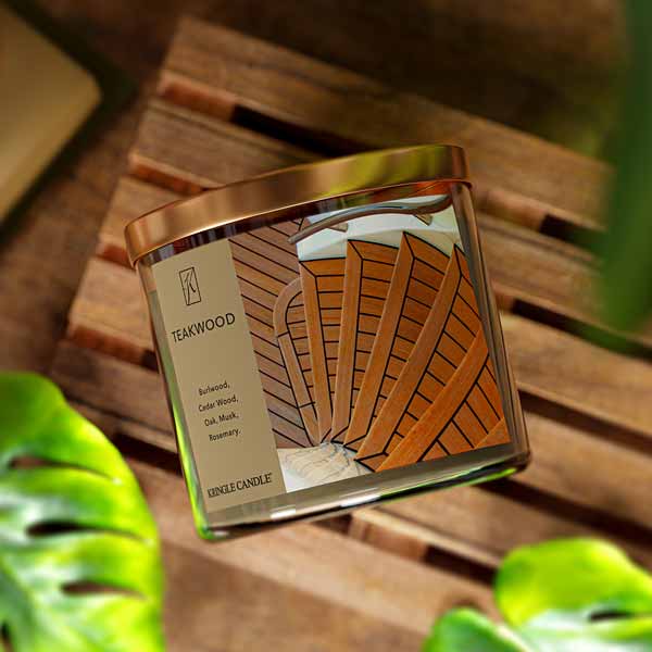 A three-wick candle in a clear glass jar with a black lid and a sophisticated wood-themed label. The label features a polished teakwood surface with an elegant woodgrain pattern. The candle’s wax is rich brown, and the wicks are unlit. The scent notes listed are burlwood, cedarwood, oak, musk, and rosemary.