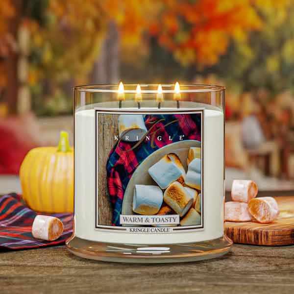 Kringle Candle Warm & Toasty 4-wick candle with marshmallow graphic on a wooden table with pumpkins and autumn leaves in the background