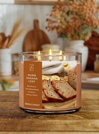 Kringle Candle with 'Warm Banana Loaf' scent on a wooden surface with bread and bananas on the label and fall background.