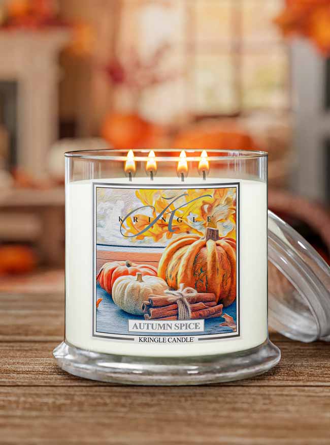 Four-wick candle labeled 'Autumn Spice' with a pumpkin-themed label on a wooden surface.