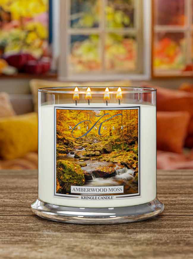 Lit XL 4-wick candle, Amberwood Moss. Label features an autumn forest with a flowing stream among mossy rocks.