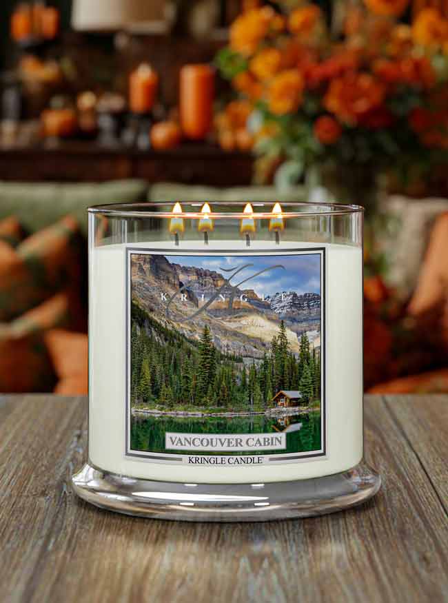 Four-wick candle lit, featuring a scenic label of a lakeside cabin surrounded by trees and mountains,  "Vancouver Cabin"