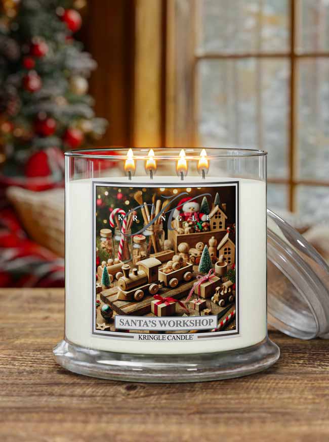 Kringle Candle Santa's Workshop candle on a wooden surface with a Christmas tree in the background