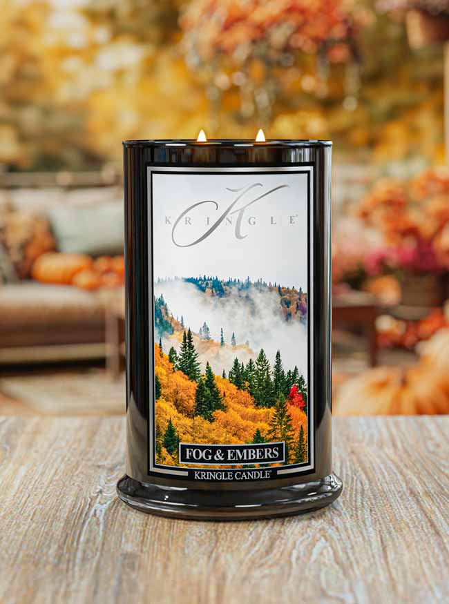 Kringle Candle with 'Fog & Embers' packaging on a wooden surface with blurred autumn decorations in the background.