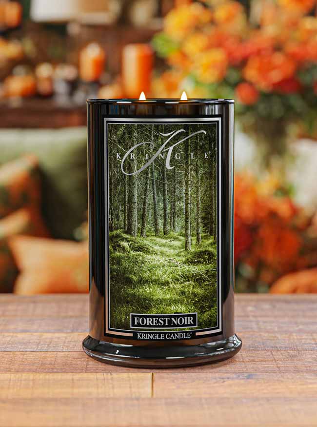 Kringle Candle Forest Noir candle on a wooden surface with a blurred autumn-themed background.