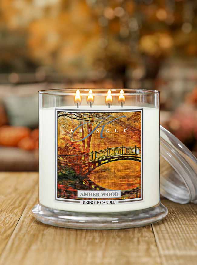 Kringle Candle lit Amber wood candle with a scenic label on a wooden surface.