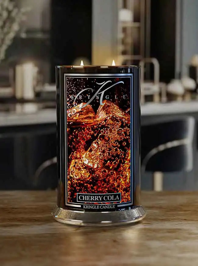 Cherry Cola scented candle by Kringle Candle, lit with two flames, placed on a wooden counter in a modern kitchen setting.