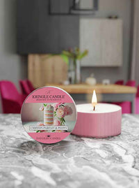 A pink candle labeled "Kringle Candle, Chiffon Parfait & Peony" sits on a marble surface, lit, with a blurred background.