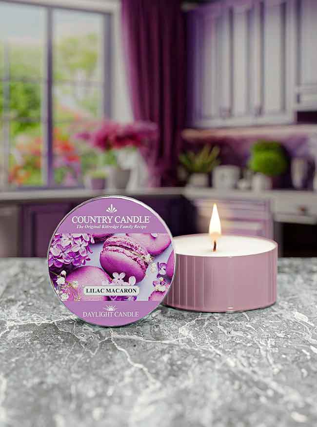 A lit lilac macaron scented candle on a marble countertop with a kitchen background.