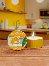 A lit candle labeled "Country Candle, Mandarin Petals" on a wooden surface in a bright, yellow-themed kitchen.