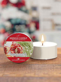Red tin for "Pomegranate & Fir" candle, next to a lit white candle on a wooden surface with a blurred festive background.