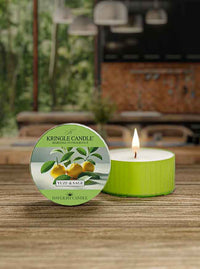 A lit green candle labeled "Kringle Candle, Yuzu & Sage" on a wooden surface, blurred indoor background.