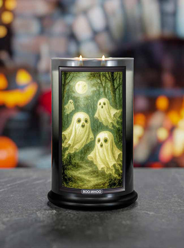 Halloween-themed Boo-Whoo candle with ghost design on a dark surface, blurred pumpkins and jack-o'-lanterns in the background.