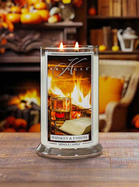 Lit 2-wick candle with label depicting a fireplace, whiskey glass, and book. Fragrance: Whiskey & Embers.