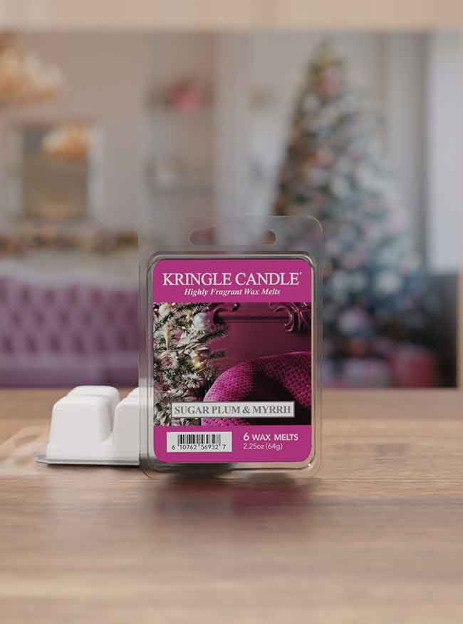 Kringle Candle wax melts labeled "Sugar Plum & Myrrh" on a table, with a blurry Christmas tree in the background.