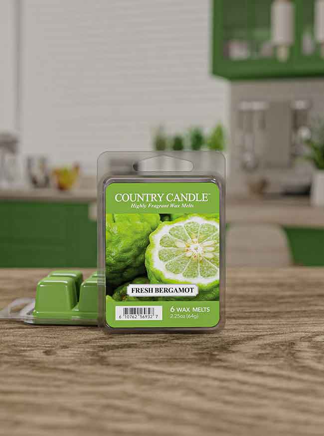 Green wax melts labeled "Country Candle: Fresh Bergamot" on a wooden table with a blurred kitchen background.