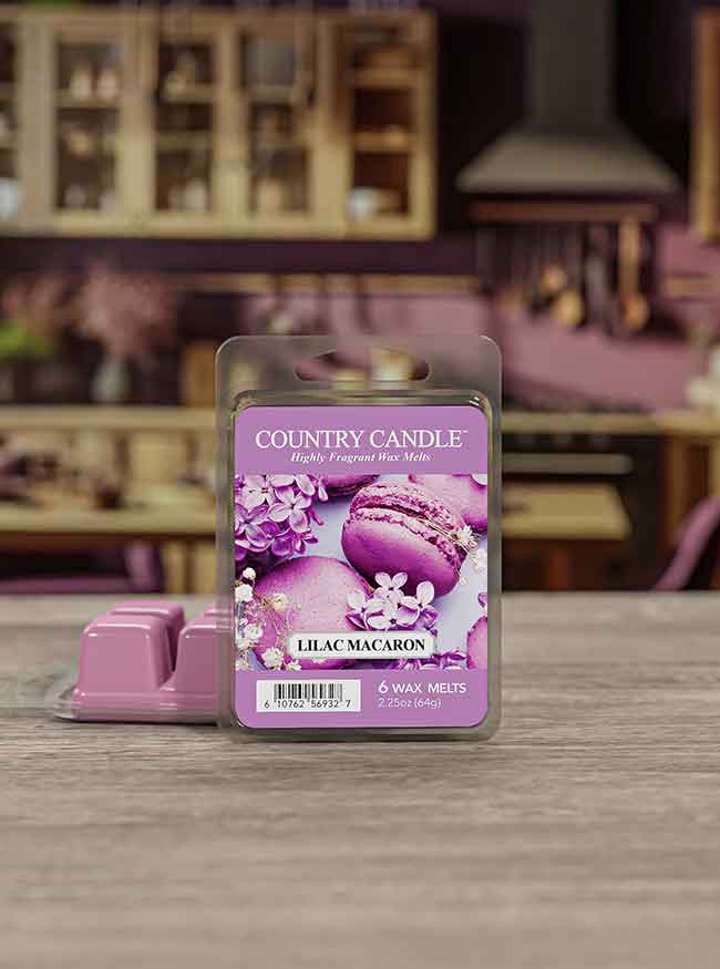 Lilac macaron scented wax melts package on a wooden table. Blurred kitchen background with cabinets and utensils.