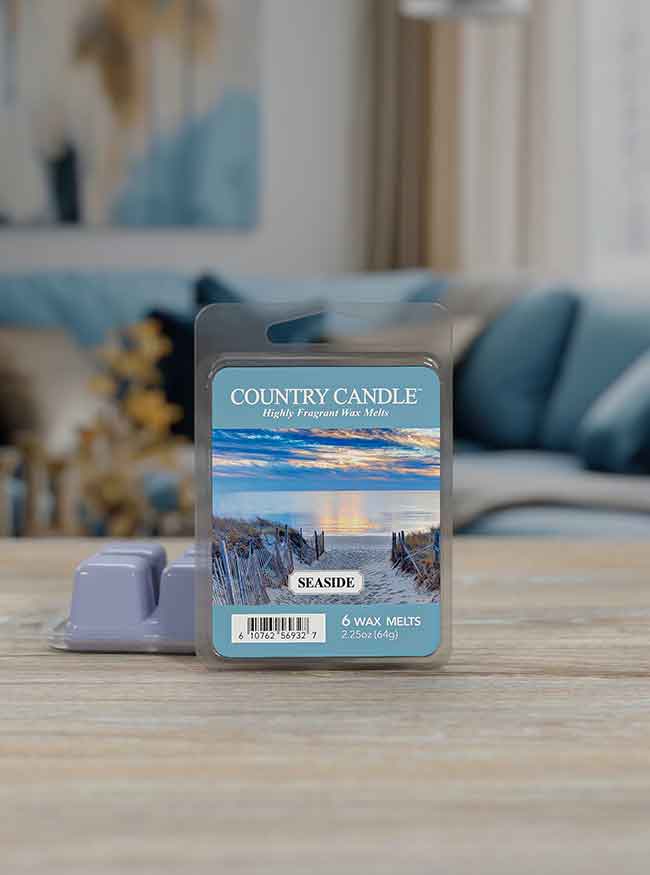 Country Candle wax melts in Seaside scent on a table, with a coastal image on the packaging; blurred living room background.