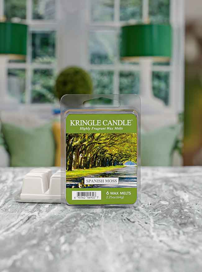 Pack of Kringle Candle Spanish Moss wax melts on a textured surface with a blurred, green-themed room in the background.